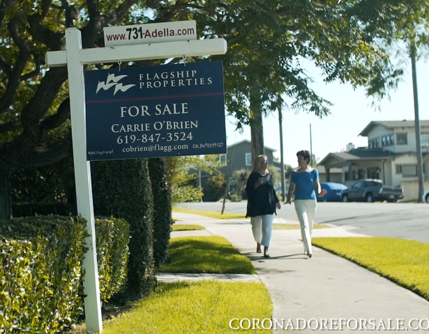 A real estate sign by the road with two women walking in the background